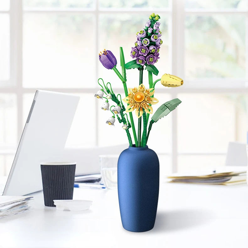 A vase filled with a floral bouquet made of building blocks featuring purple and yellow flowers on a white desk.