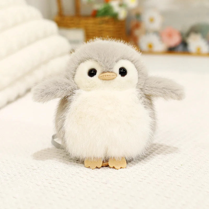 A fluffy gray and white cartoon bird plush keychain with large eyes resting on a white surface.