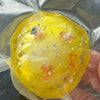 A yellow stress ball is visible inside a clear plastic bag, showing its texture and color.