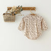 A vintage floral baby girl outfit set featuring a light-colored blouse and romper hanging on a wooden hanger.