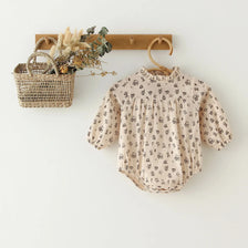 A vintage floral baby girl outfit set featuring a light-colored blouse and romper hanging on a wooden hanger.