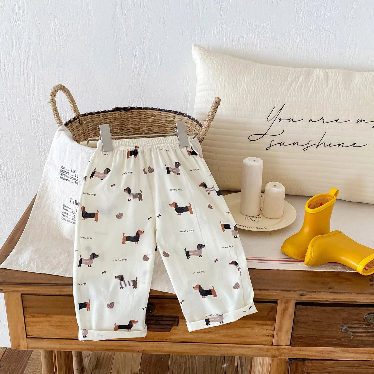 Cream casual pants with a plaid print featuring small dog illustrations displayed on a wooden surface.
