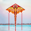 Un cerf-volant delta orange et jaune en forme de dragon, affiché contre un ciel doux et de l'eau bleue.