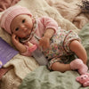 A realistic soft silicone reborn baby doll wearing a pink outfit, resting on a cream-colored knitted blanket.