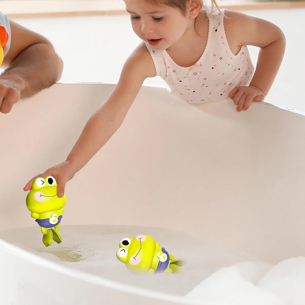 A young girl is placing a yellow swimming frog toy into a white bathtub.