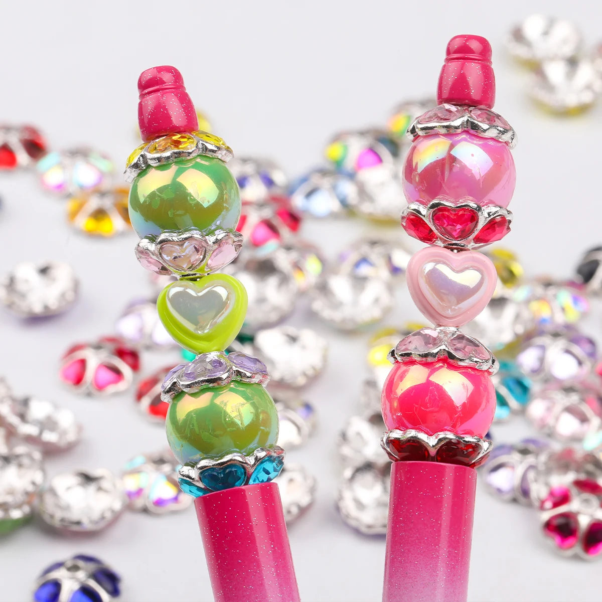 A close-up of pink and iridescent heart-shaped rhinestone flower charm beads stacked on a pink and purple plastic tube.