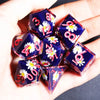 A hand holds a set of handmade resin polyhedral dice featuring pink and white floral designs.