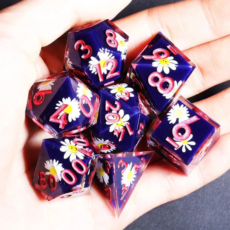 A hand holds a set of handmade resin polyhedral dice featuring pink and white floral designs.