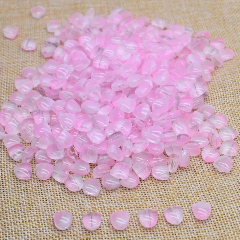 A pile of pink tulip flower glass beads scattered on a beige fabric surface.