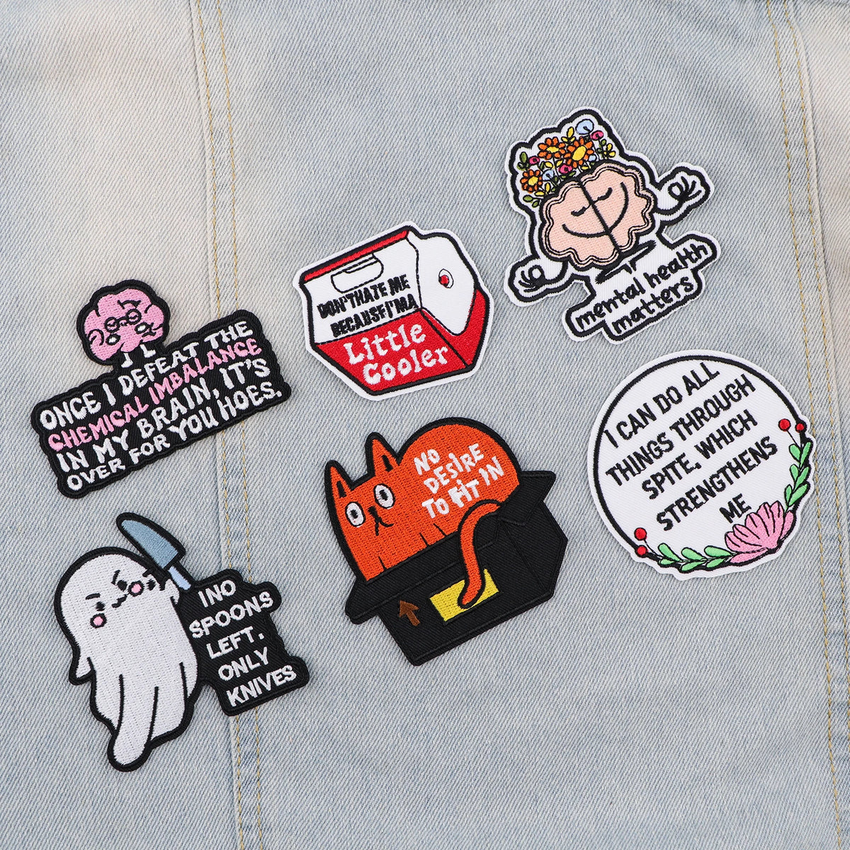 A collection of embroidered patches featuring quotes about mental health, self-worth, and resilience on a light denim fabric.