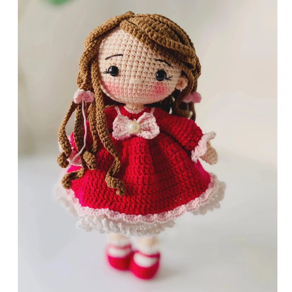 A handmade crochet doll with brown hair and a red dress and white trim.