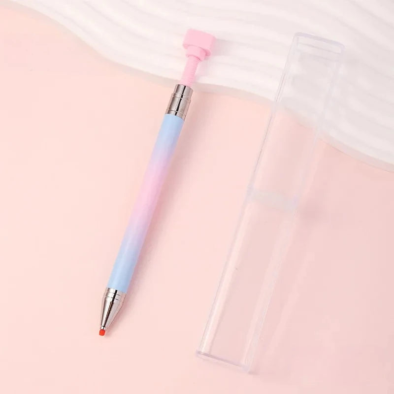 A refillable gradient diamond picking pen with a pink and blue gradient barrel and a pink wax tip resting on a light pink sur