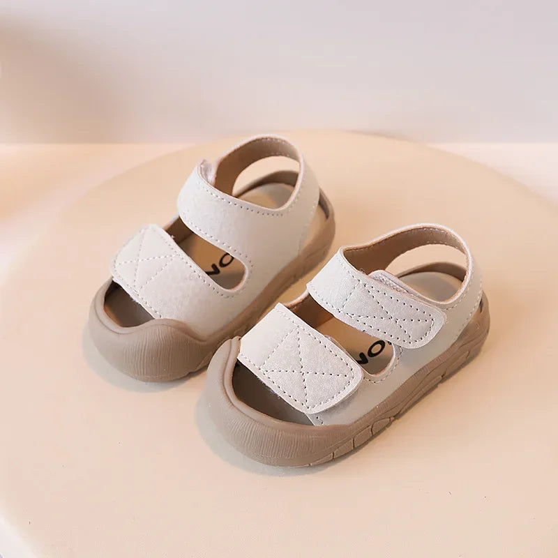 A pair of light beige toddler soft-soled sandals for boys and girls resting on a neutral background.