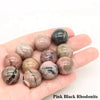 A collection of pink and black rhodonite crystal spheres held in a person's hand.