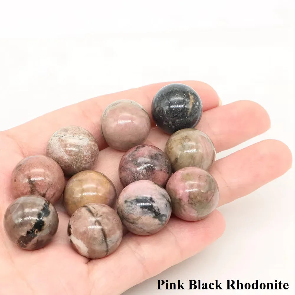 A collection of pink and black rhodonite crystal spheres held in a person's hand.
