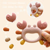 A pink crab-shaped silicone baby teether for soothing gums, shown in a hand.