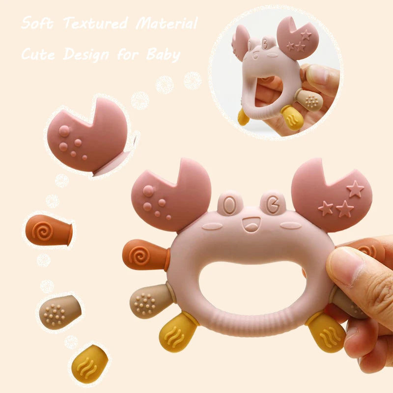 A pink crab-shaped silicone baby teether for soothing gums, shown in a hand.