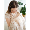 A woman wearing a beige breathable muslin nursing cover with a delicate pattern, looking down.