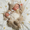 A realistic 18-inch vinyl reborn baby doll wearing a bear outfit is lying on a white blanket.