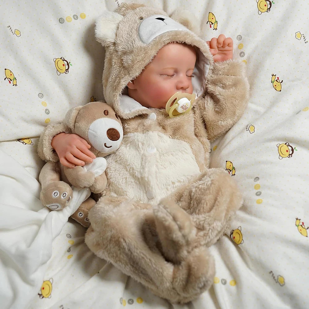 A realistic 18-inch vinyl reborn baby doll wearing a bear outfit is lying on a white blanket.