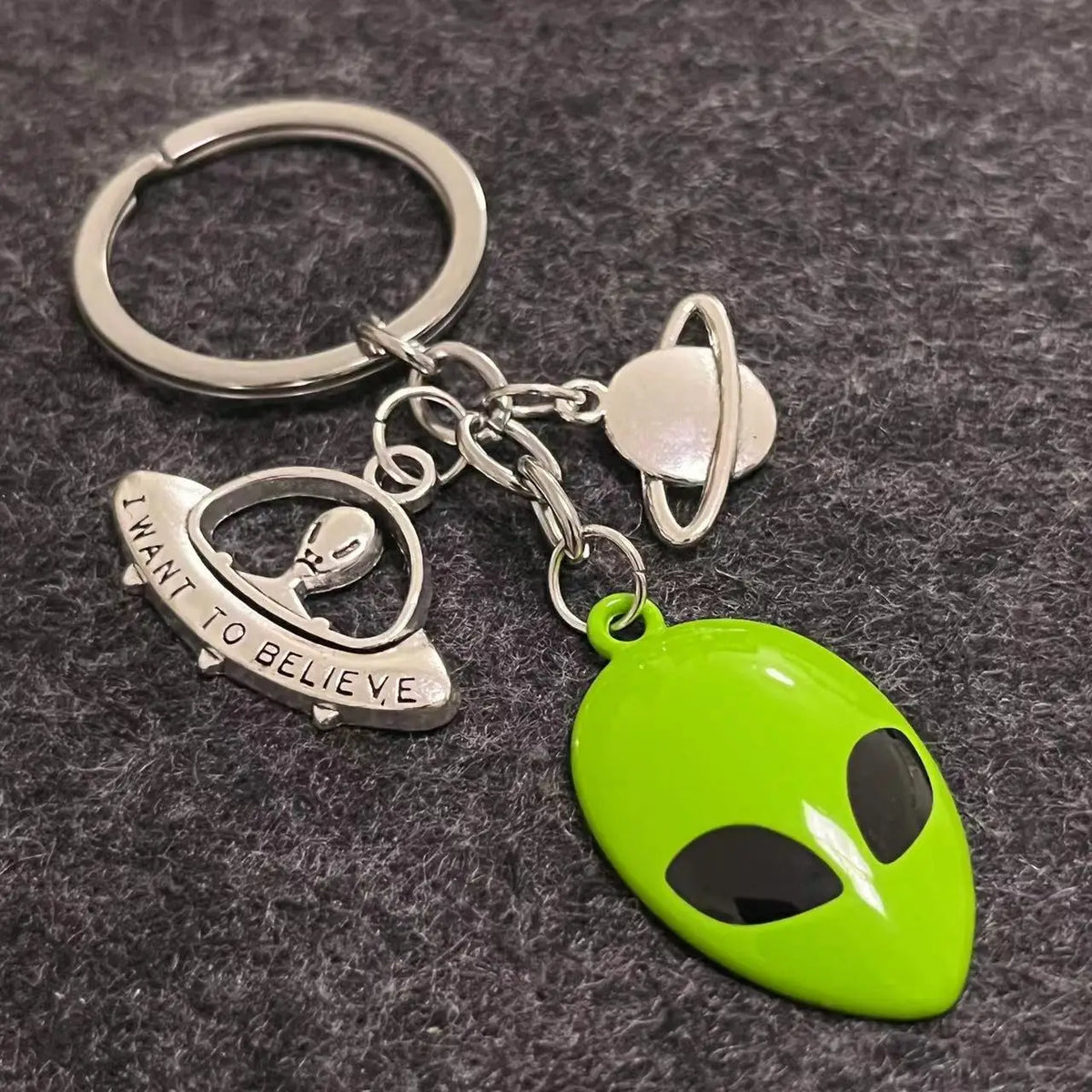 Silberner Schlüsselanhänger mit grüner Alien-Maske und schwarze Augen sowie silbernem Planeten-Anhänger.