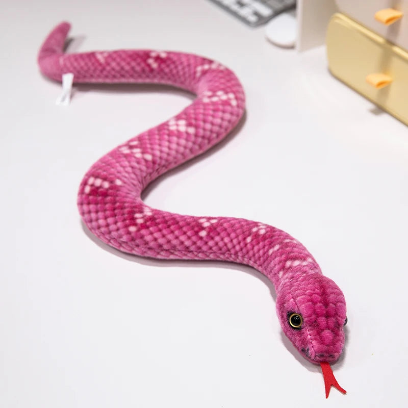 A pink simulation snake plush toy with a textured body and a red tip is lying on a white surface.