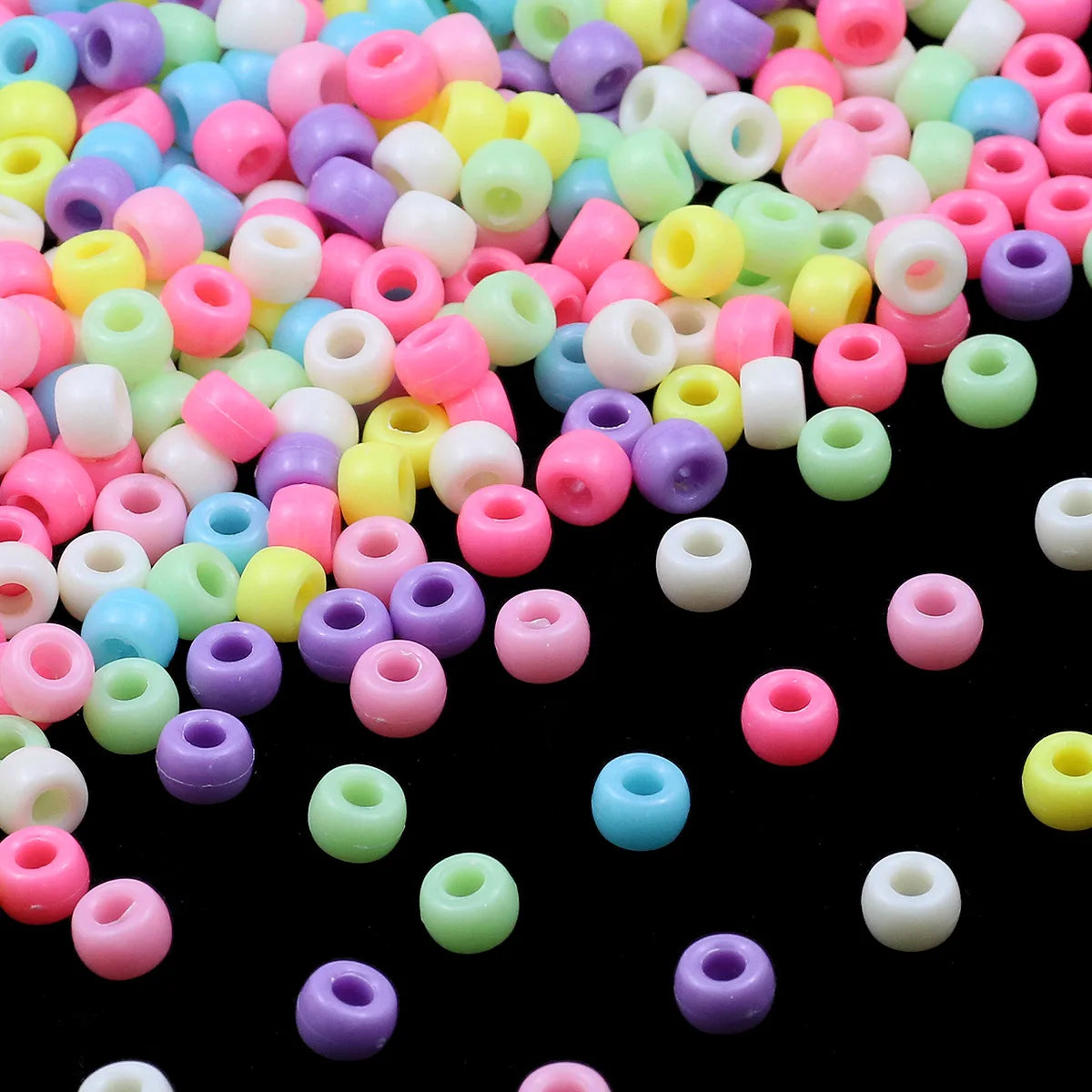 A close-up view of a large pile of multicolor pony beads in various shades of pink, green, yellow, and purple.