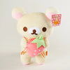 A fluffy white Rilakkuma bear plush toy with a pink strawberry accessory and a pink tag.