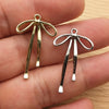 A pair of gold and silver alloy bow charms for jewelry making displayed on a hand.