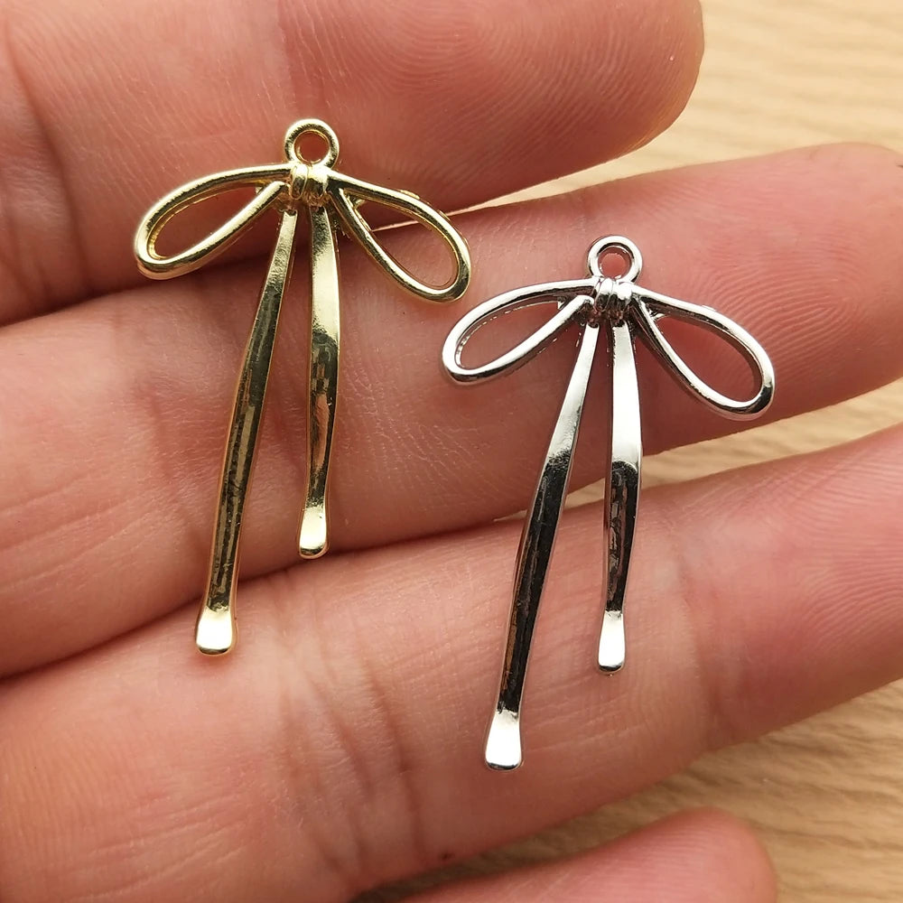A pair of gold and silver alloy bow charms for jewelry making displayed on a hand.