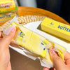 A hand holds a yellow squishy butter bar stress relief toy with white packaging.
