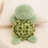 A soft, light green plush toy of a sea turtle with textured skin and small feet resting on a white towel.