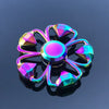 A colorful metal fidget spinner with a flower design is reflected on a dark surface.