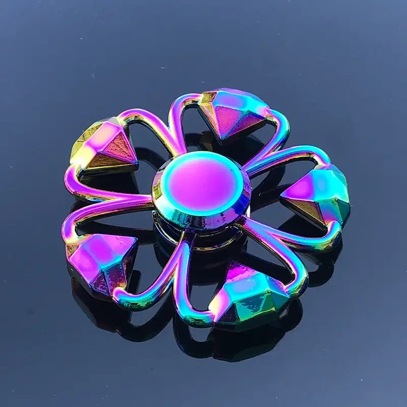 A colorful metal fidget spinner with a flower design is reflected on a dark surface.