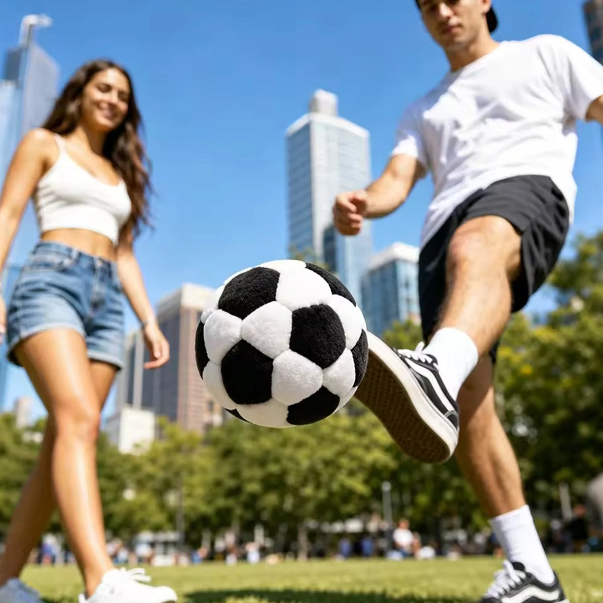 A man in a white shirt is kicking a black and white soccer ball on a grassy field with a woman nearby.
