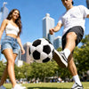 A man is kicking a black and white soccer ball on a grassy field with a woman in the background.
