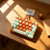 An orange keyboard keycap clicker keychain with various colored keycaps and a small rose is displayed on a wooden surface.