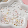 A white silicone mold contains a large quantity of small, round imitation jade glass spacer beads in various translucent and 