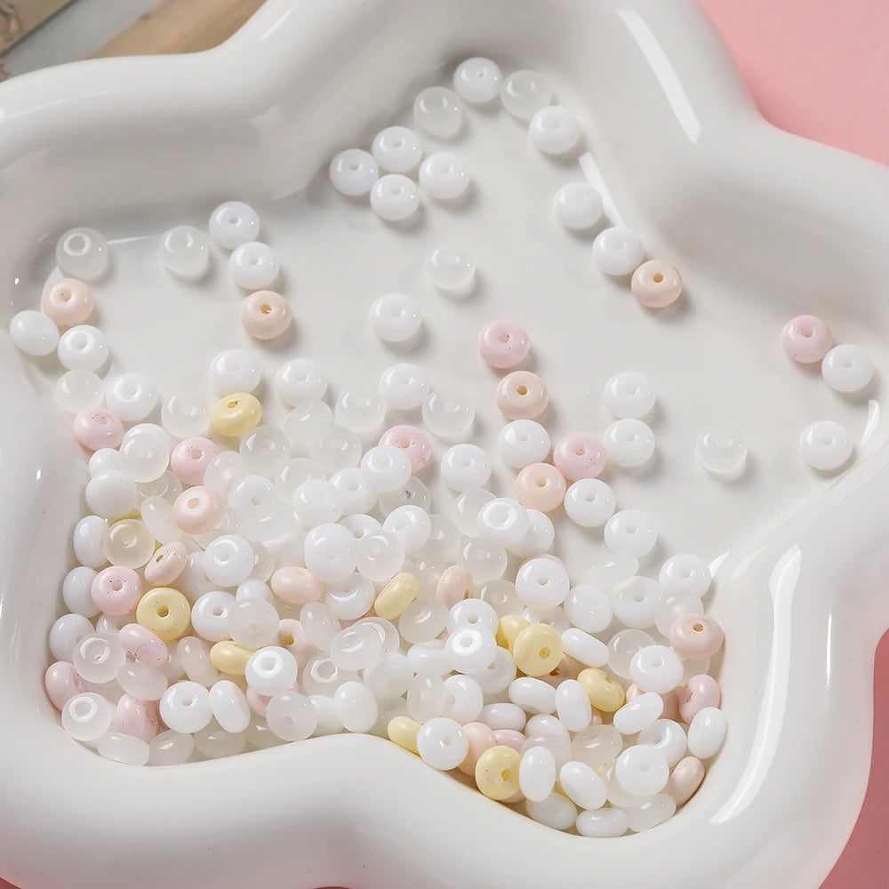 A white silicone mold contains a large quantity of small, round imitation jade glass spacer beads in various translucent and 
