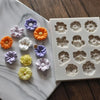 A collection of silicone flower molds in various shades of orange, purple, and white are displayed on a white marble surface.