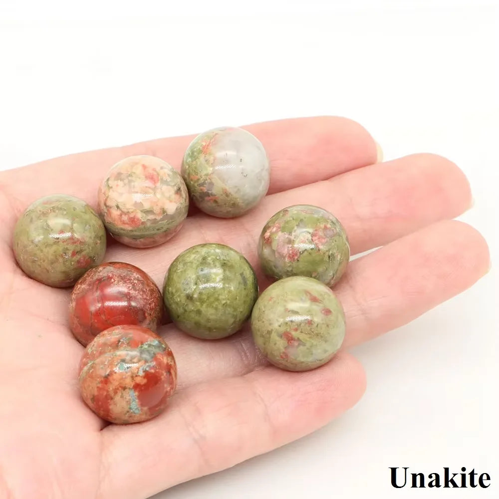 A hand holds several polished crystal spheres displaying natural shades of green, pink, and reddish-brown.