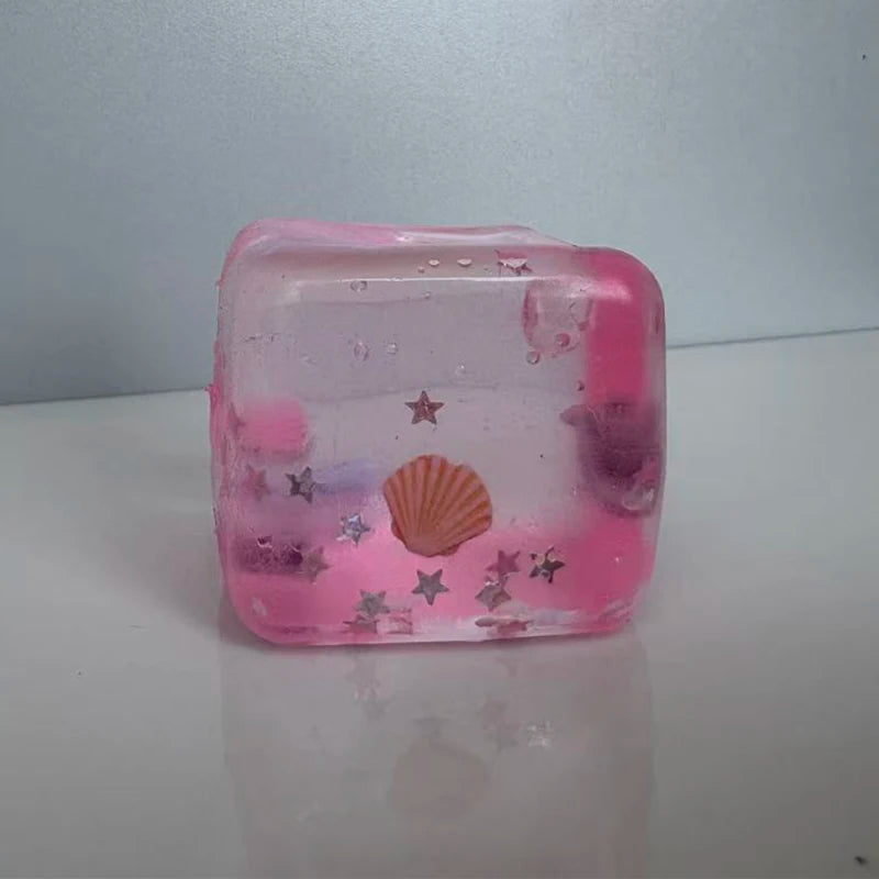 A translucent pink squishy stress ball shaped like a cube, decorated with stars and a seashell.