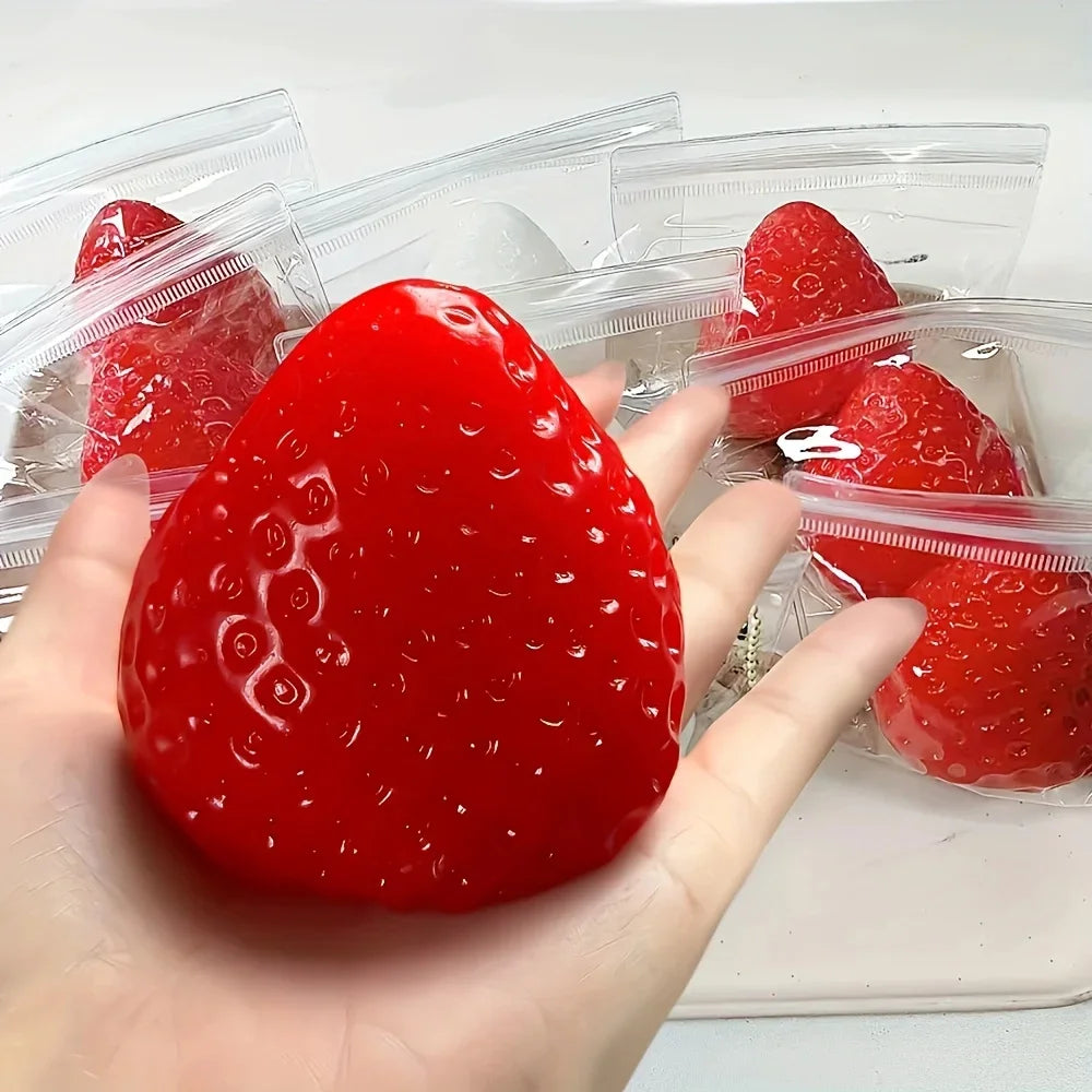 A hand holds a bright red strawberry squishy fidget toy packaged in clear plastic bags.