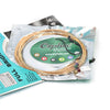 A spool of bronze acoustic guitar strings is shown inside a clear plastic bag with a green label.