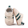 A pair of beige baby first walkers soft sole shoes with green stripes and a light tan interior.