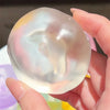 A hand holds a clear, iridescent fidget ball with a soft pink and white gradient color.