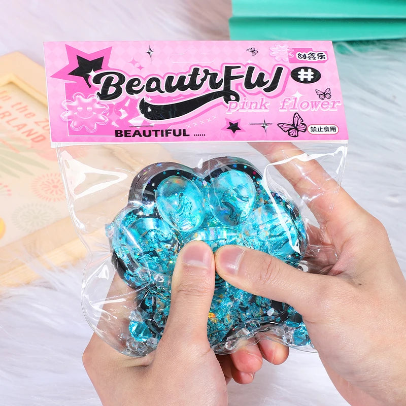 A hand holds a translucent blue cat paw squishy fidget toy packaged with a pink label.