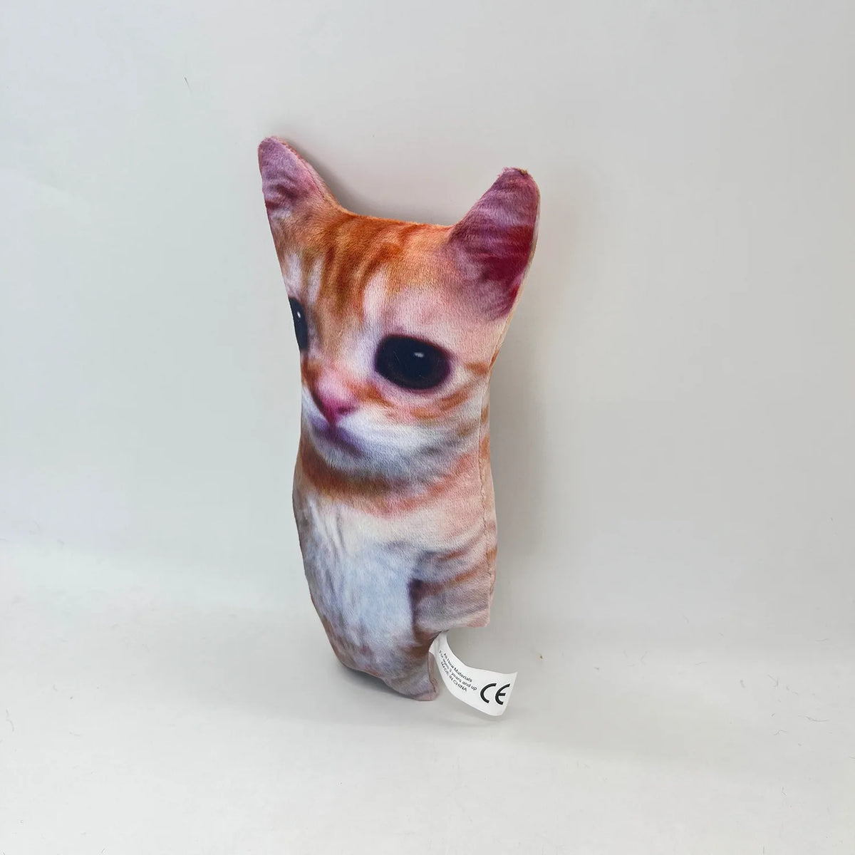 A small, plush cat doll with orange and white fur and large eyes is displayed against a plain white background.
