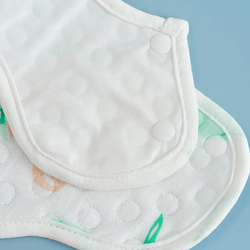 A close-up view of a white baby bib with a quilted texture and small buttons, lying next to another similar bib.