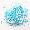 A white bowl filled with blue and white polymer clay sprinkles scattered on a white surface.